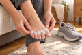 A close-up of a person's hands applying a white toe spreader pad to their toes, with gray athletic sneakers resting on a textured rug in the background.